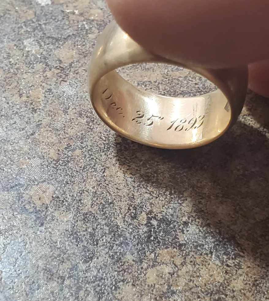 A close-up of a ring being held, showing an inscription inside that reads "Dec. 25 1892"