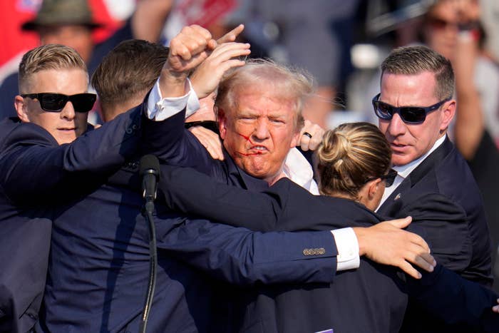 Donald Trump surrounded by security personnel, with a noticeable injury on his face