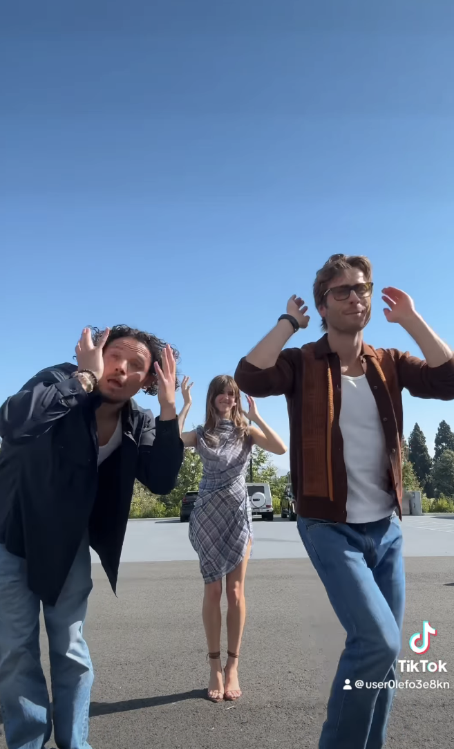 Anthony Ramos, Daisy Edgar-Jones, and Glen Powell perform a TikTok dance outdoors. Anthony and Glen are wearing casual outfits, while Daisy is in a stylish dress