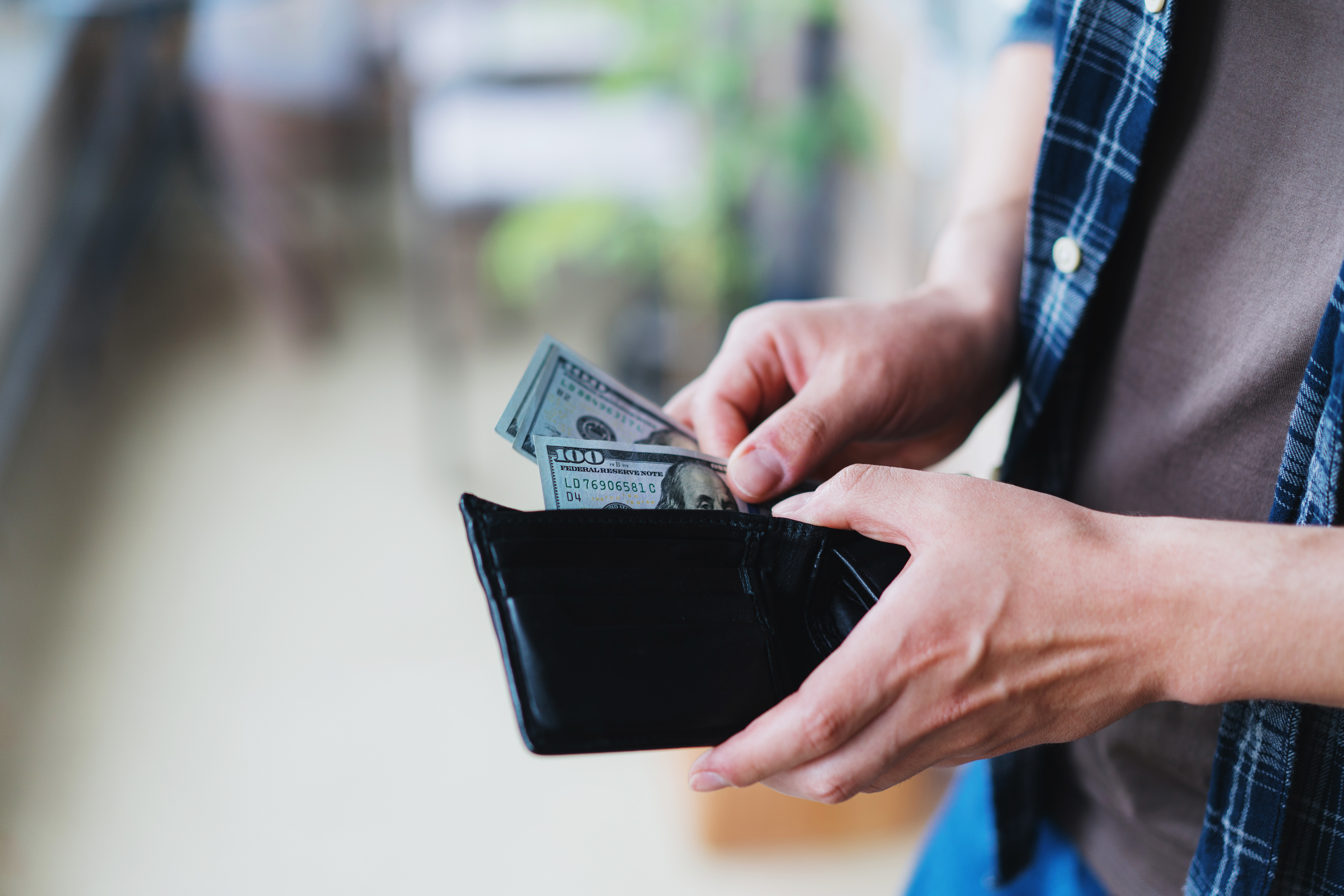 A person is holding an open wallet and placing or removing U.S. dollar bills. The person’s face is not visible