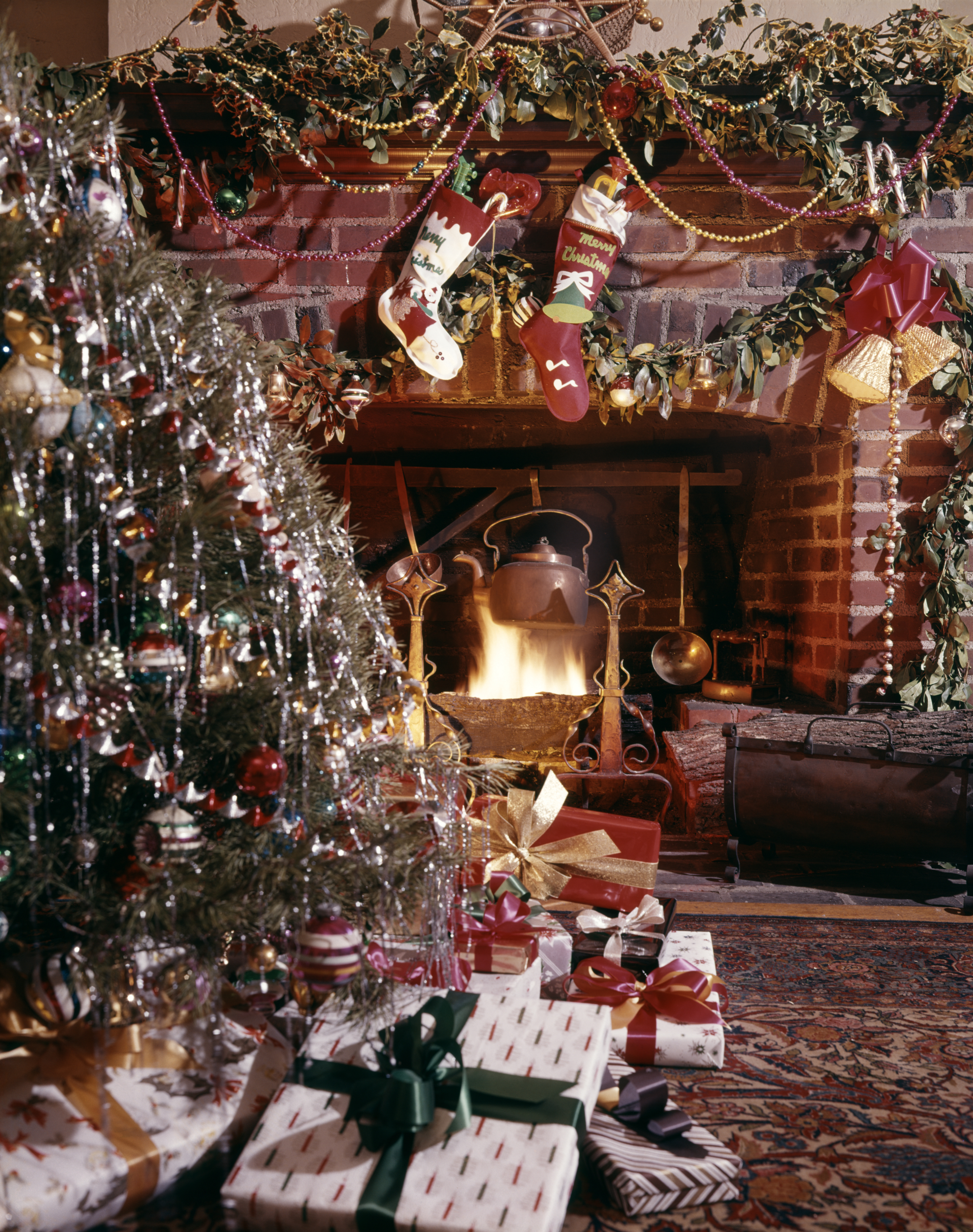 A cozy fireplace decorated with stockings, garland, and ornaments; a Christmas tree covered in tinsel and ribbons; various wrapped gifts are under the tree