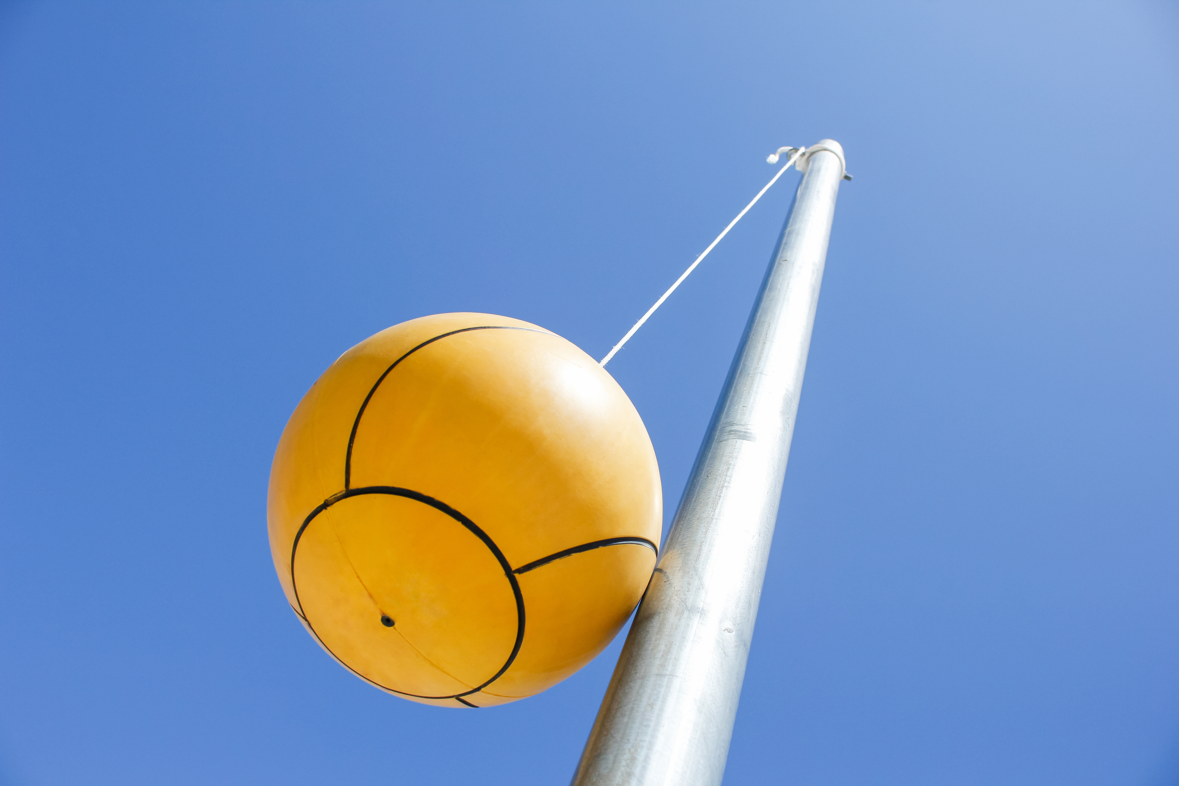 A tetherball attached to a metal pole is against a clear blue sky
