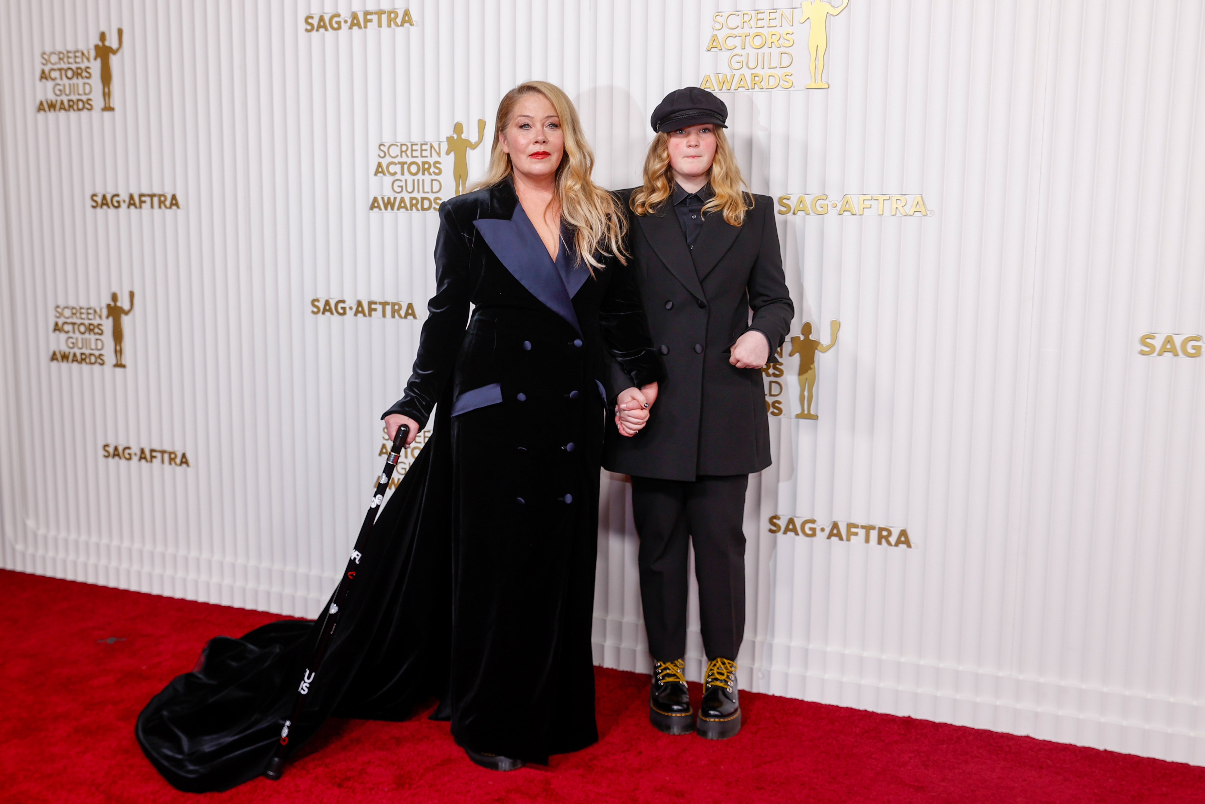 Leslie Grossman in a flowing velvet gown and her daughter Goldie James wearing a suit and cap, holding hands on the SAG Awards red carpet
