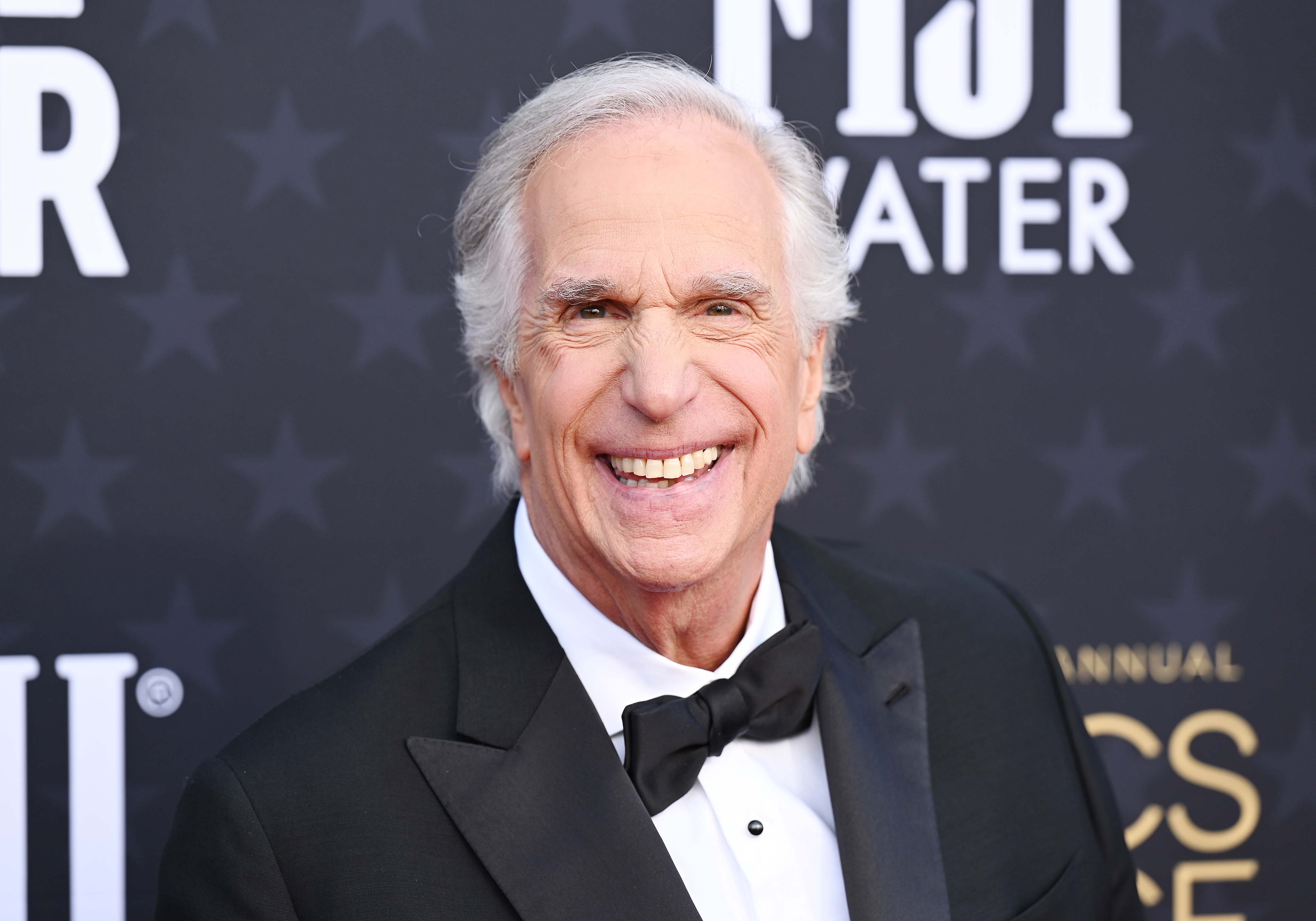 Henry Winkler smiles in a tuxedo at a red carpet event