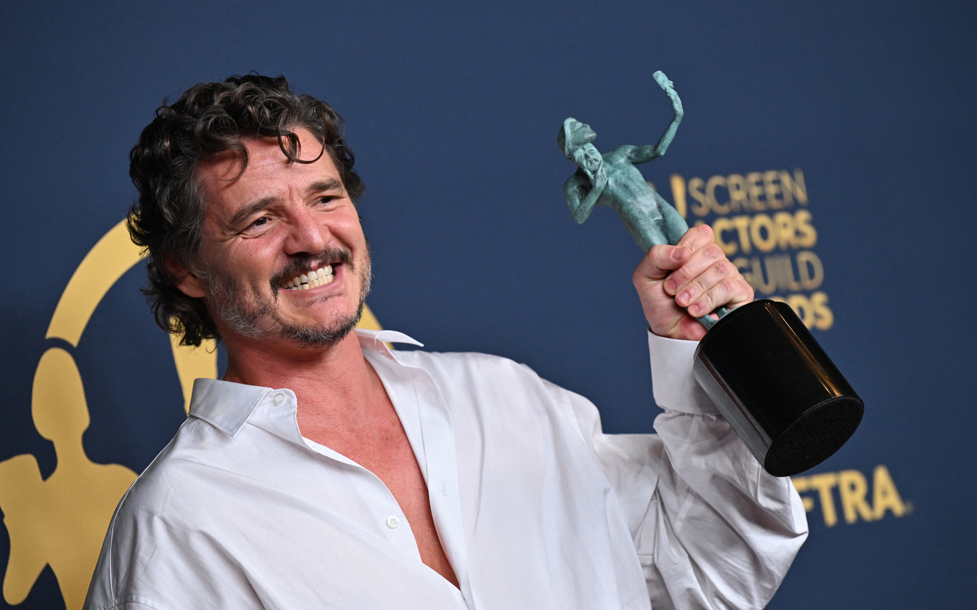 Pedro Pascal, wearing a white shirt, smiles while holding his Screen Actors Guild Award at the event