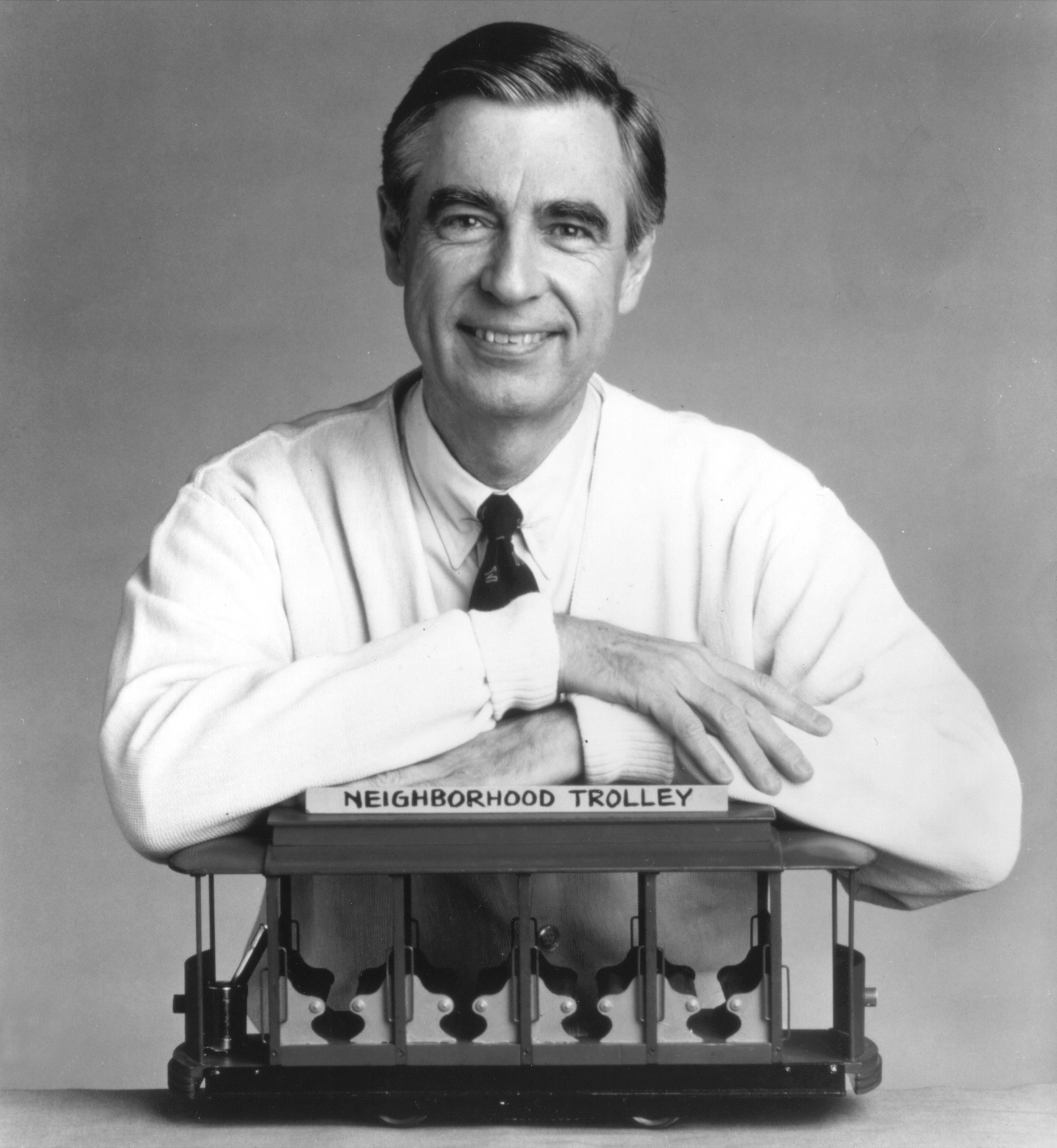 Fred Rogers smiles with arms resting on a model of the 'Neighborhood Trolley' from "Mister Rogers' Neighborhood."
