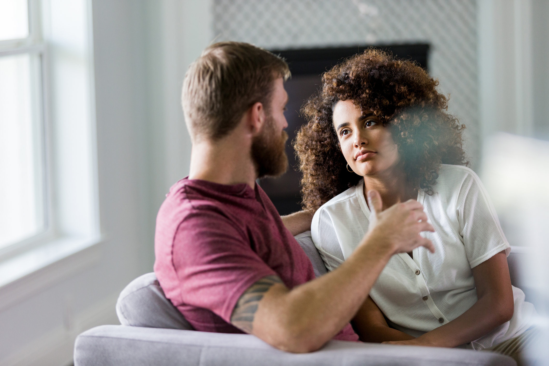 A man and a woman sit on a couch, engaged in a serious conversation