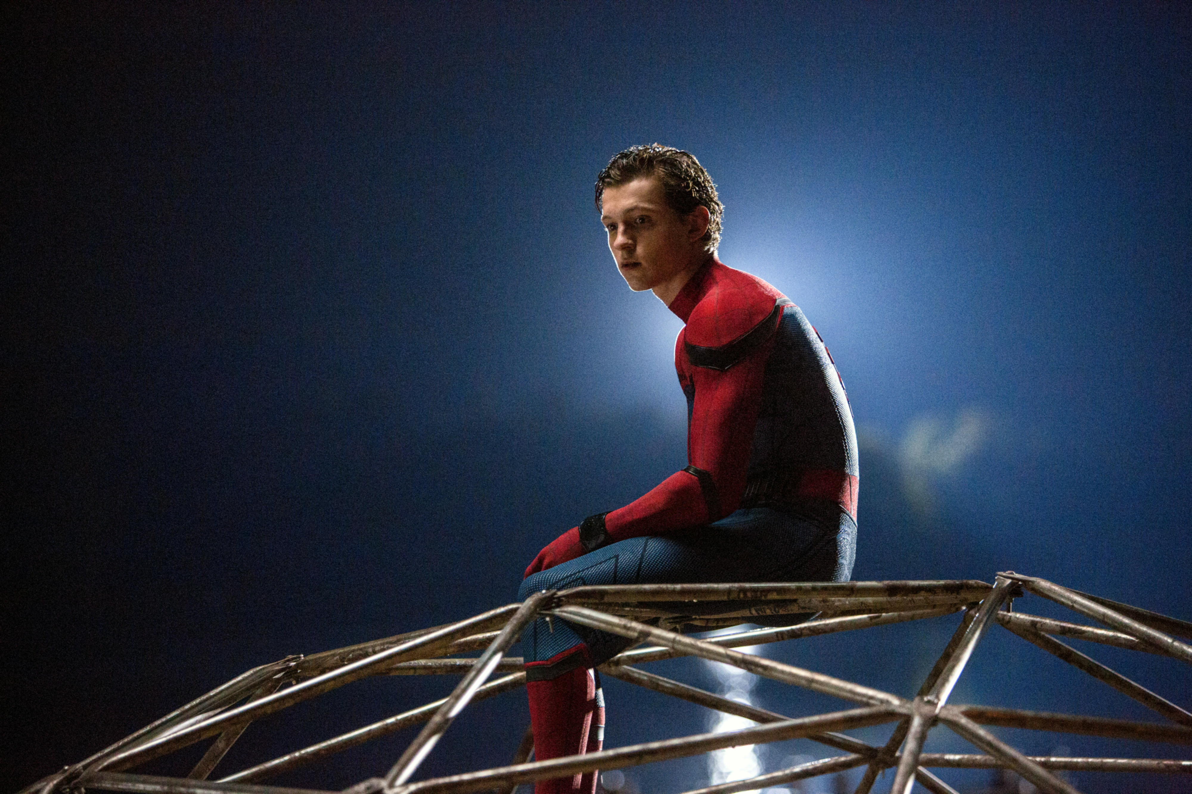 Tom Holland, dressed as Spider-Man, sits pensively atop a metal structure in a scene from "Spider-Man: Homecoming"