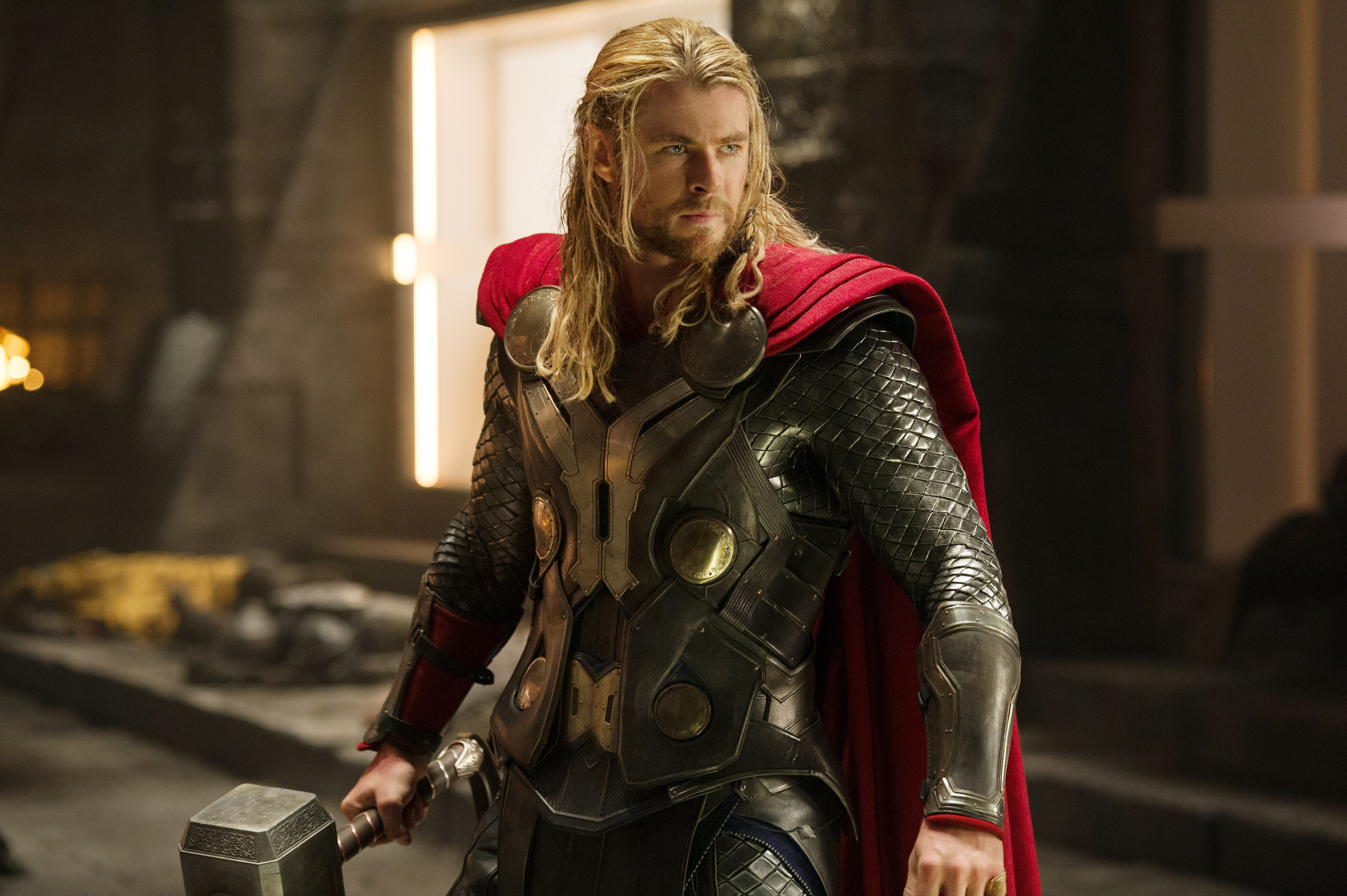 Chris Hemsworth holding a hammer, wearing a detailed armored suit with a red cape in a scene from "Thor: The Dark World"