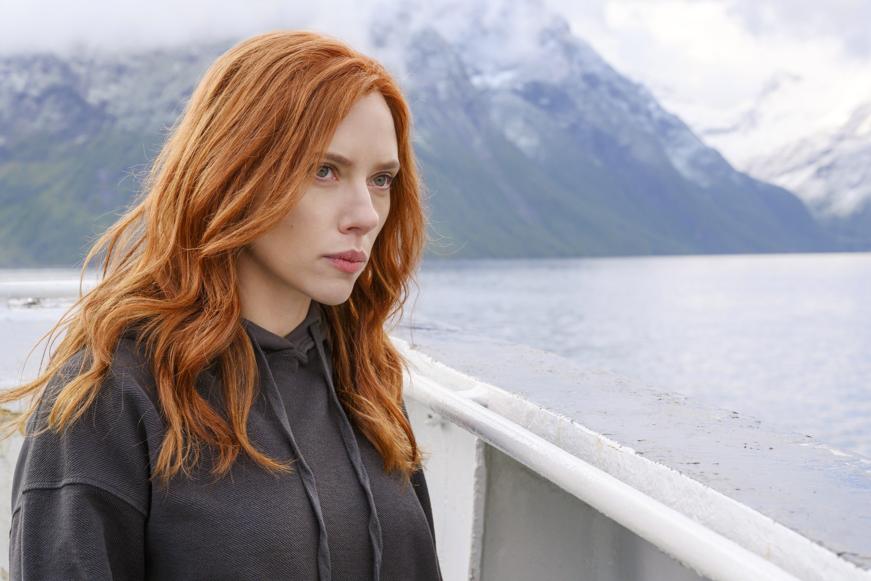 Scarlett Johansson standing by a body of water with mountains in the background in a scene from "Black Window"