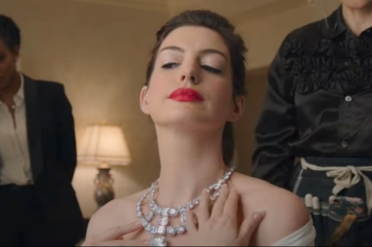Anne Hathaway admiring an intricate necklace she's wearing as Daphne in Ocean's Eight