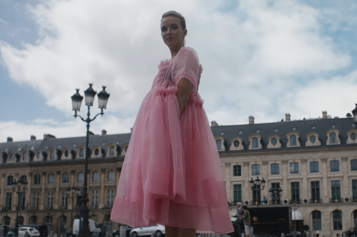 Jodie Comer stands outdoors in front of a large building in Europe as Villanelle on Killing Eve