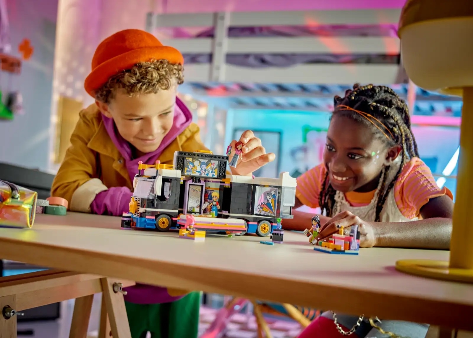 Two children smiling and playing with a colorful LEGO set on a table indoors