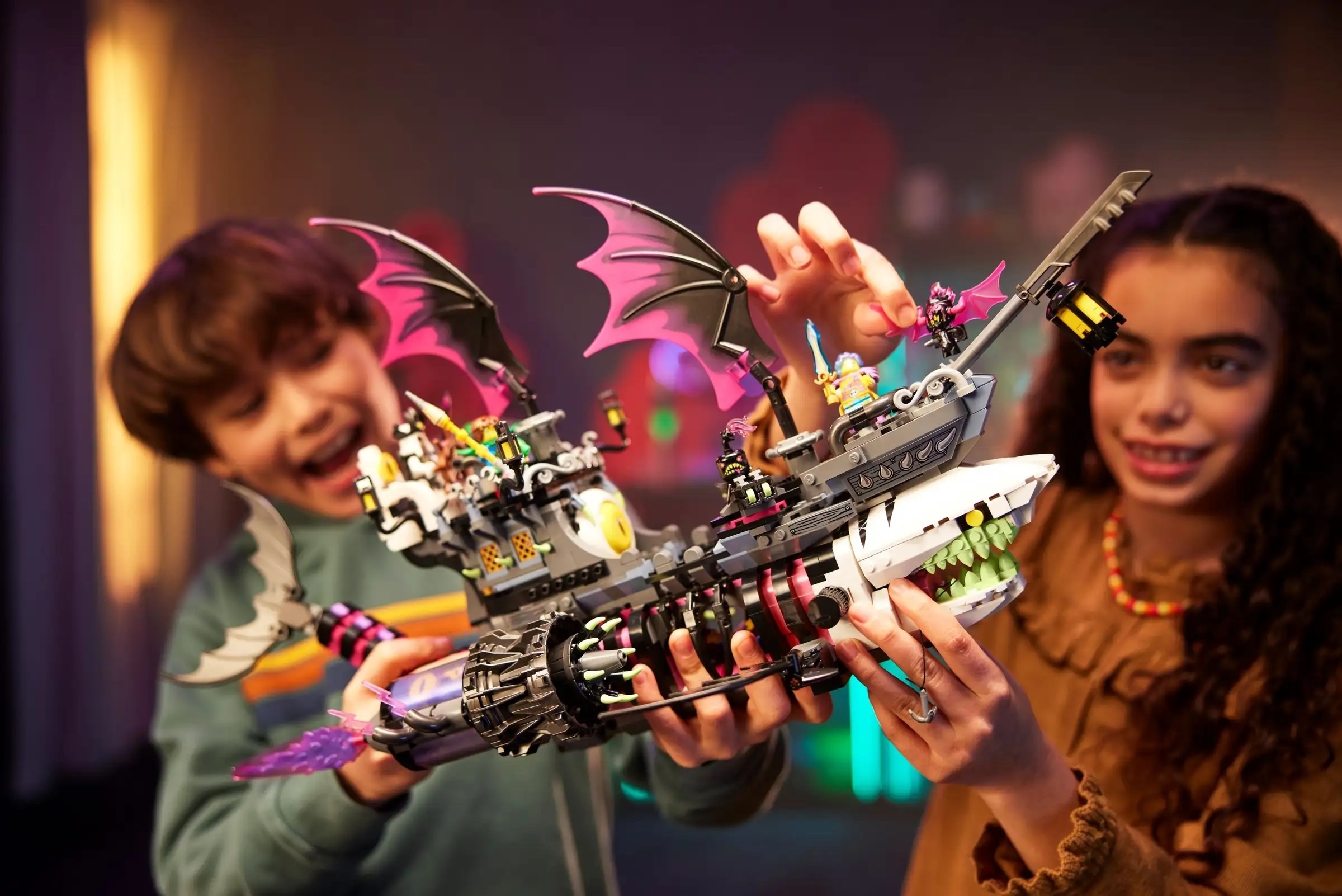 Two children play enthusiastically with a detailed LEGO pirate ship, featuring imaginative elements like bat wings and glowing neon pieces