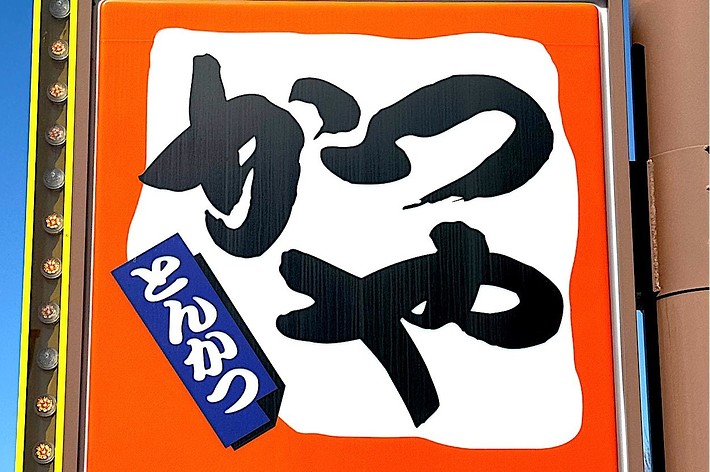Sign with Japanese text for a tonkatsu (fried pork cutlet) restaurant. The sign features large, stylized kanji characters and a blue vertical label