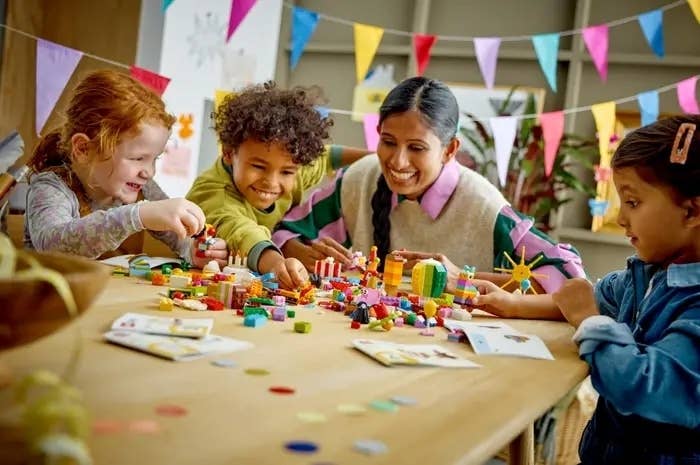 Children and an adult at a table playing with toys and LEGO pieces, surrounded by colorful decorations and bunting