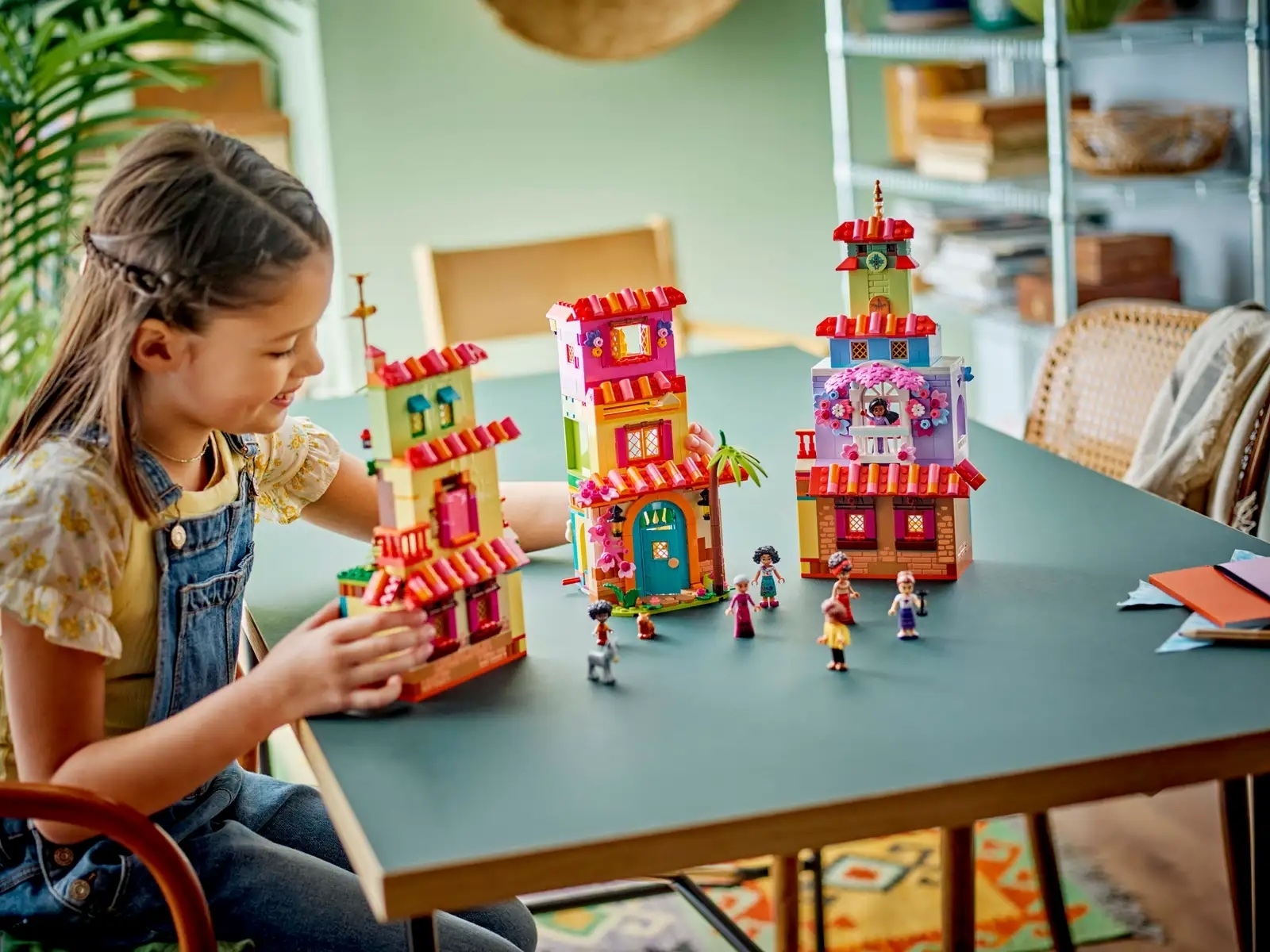 A child is playing with a colorful set of toy buildings and miniature figures on a table in a well-organized room