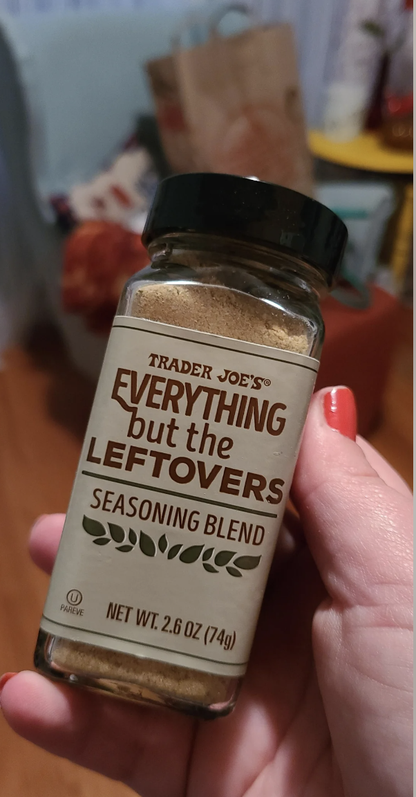 A hand holds a Trader Joe's &quot;Everything but the Leftovers&quot; seasoning blend, 2.6 oz (74g), in a home setting