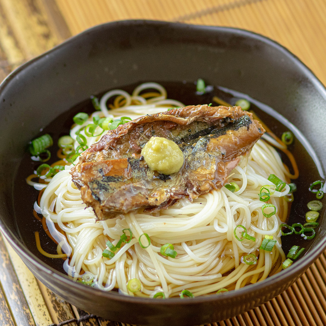 器に盛られたそばの上にさんまのかば焼きとわさびがのっている料理。細ねぎが周りに散らされている。