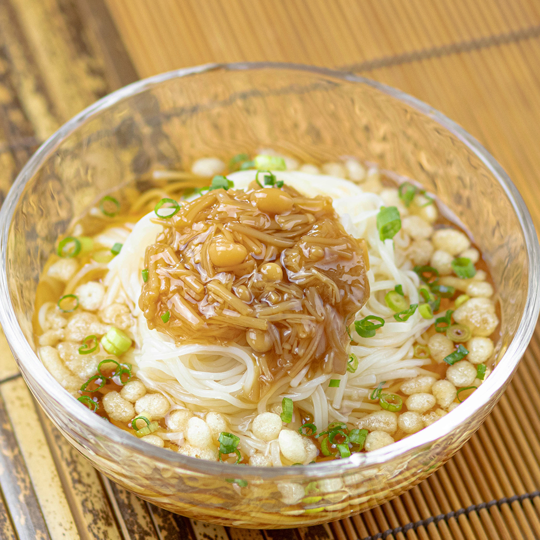 ガラスの器に盛られた日本の冷製素麺、上には刻んだネギときのこのトッピング。