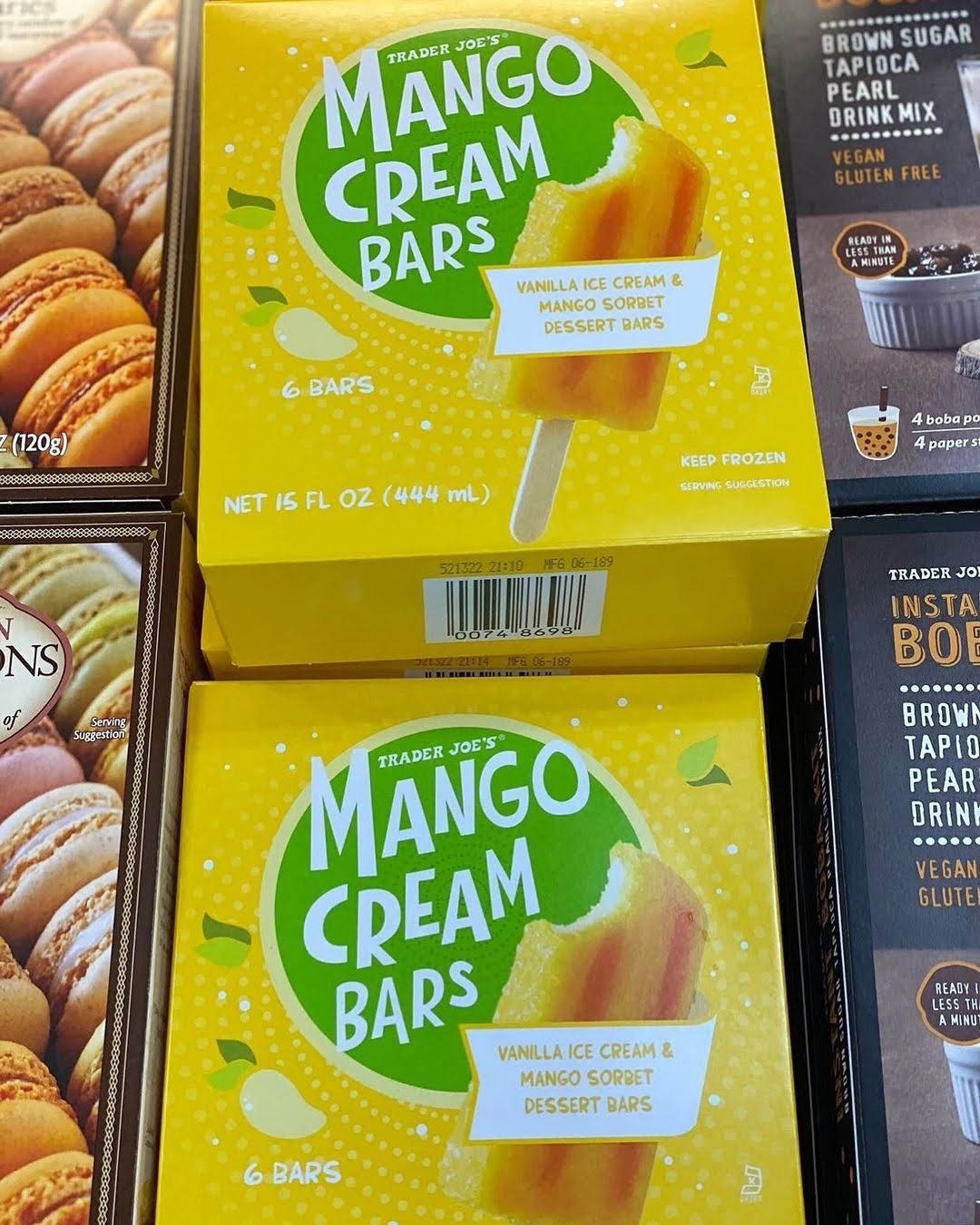 Two boxes of Trader Joe's Mango Cream Bars, featuring vanilla ice cream and mango sorbet dessert bars, are displayed next to other Trader Joe's frozen dessert boxes