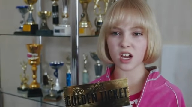 AnnaSophia Robb, wearing a sporty jacket, holds a "Golden Ticket" in front of a trophy shelf. The image relates to an article in the Work & Money category