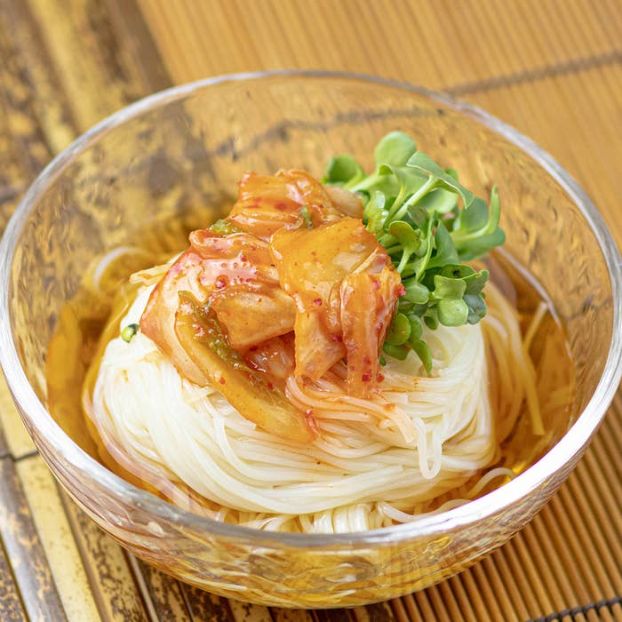 ガラス鉢に入った冷たいそうめん、キムチと野菜がのっている。
