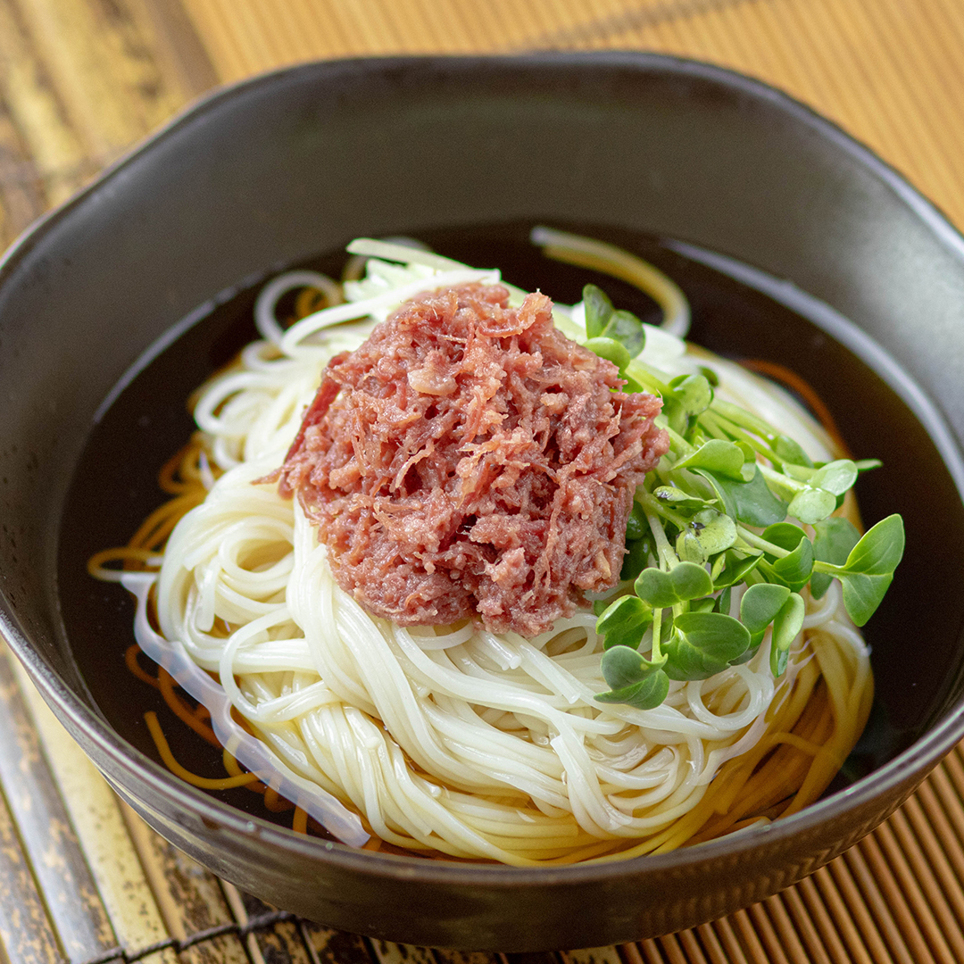器に入った冷麺の上に細かくほぐされた肉と緑の葉が盛り付けられている料理。