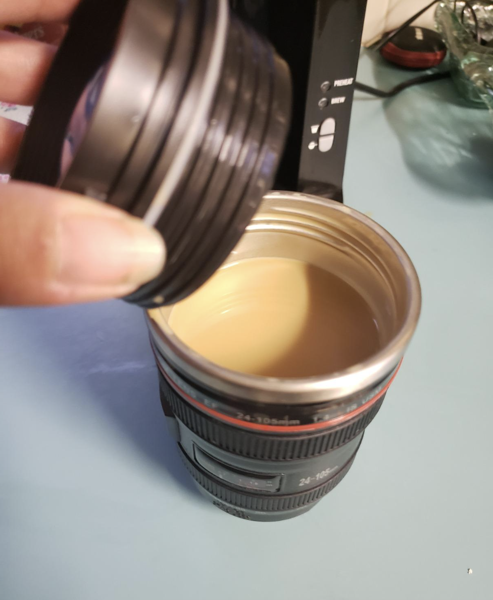 Hand holding a lens-shaped coffee mug filled with a light-colored beverage