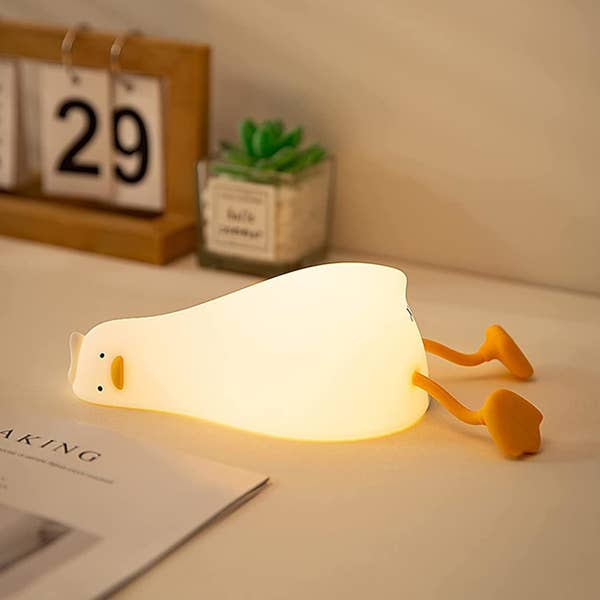 Duck-shaped lamp lying on a table with calendar, plant, and open book in the background