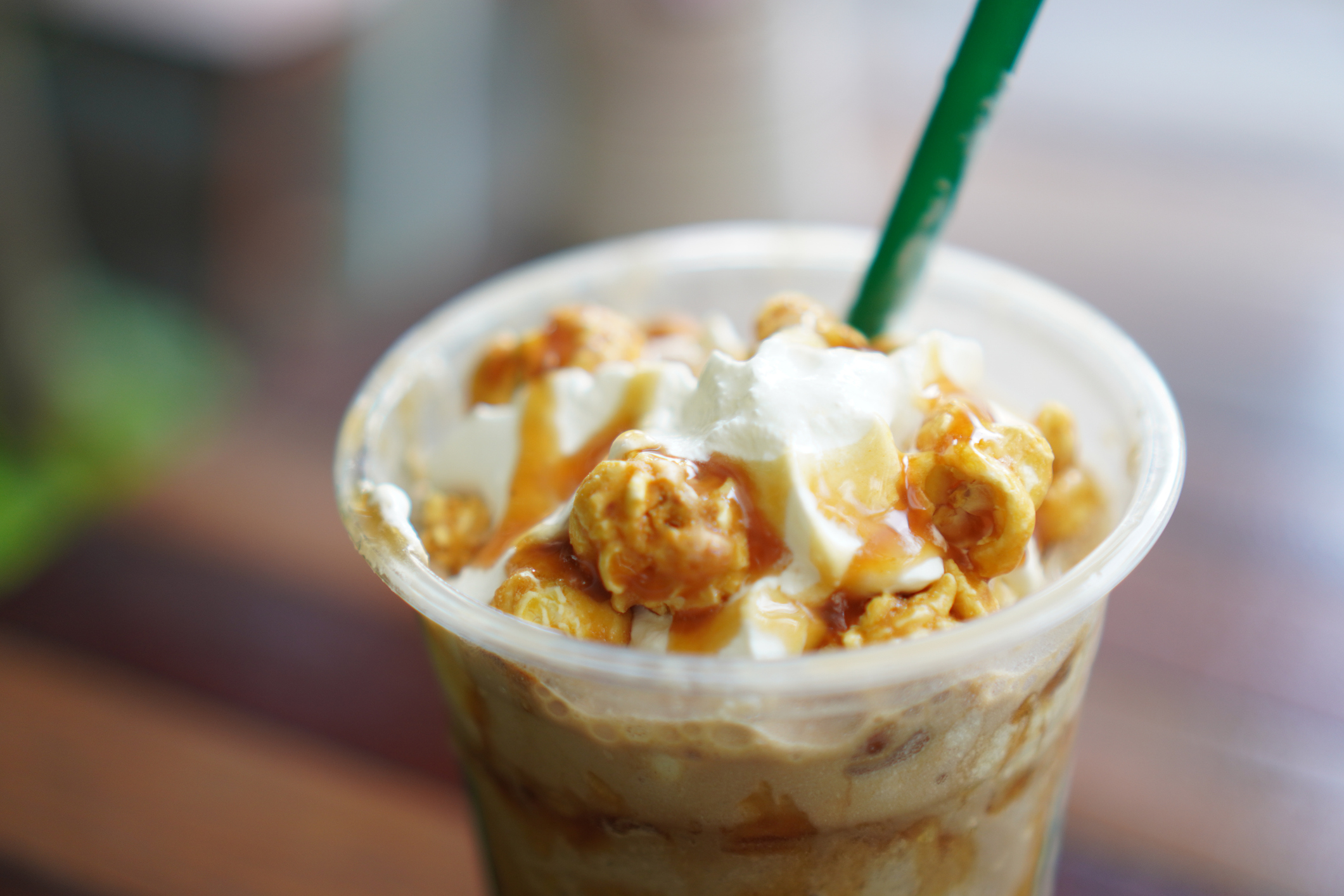 Close-up of a caramel popcorn and whipped cream-topped iced coffee with a green straw