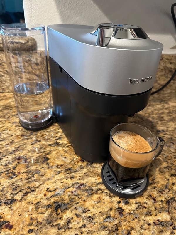 Nespresso coffee machine on a kitchen counter with a glass of brewed coffee placed in front