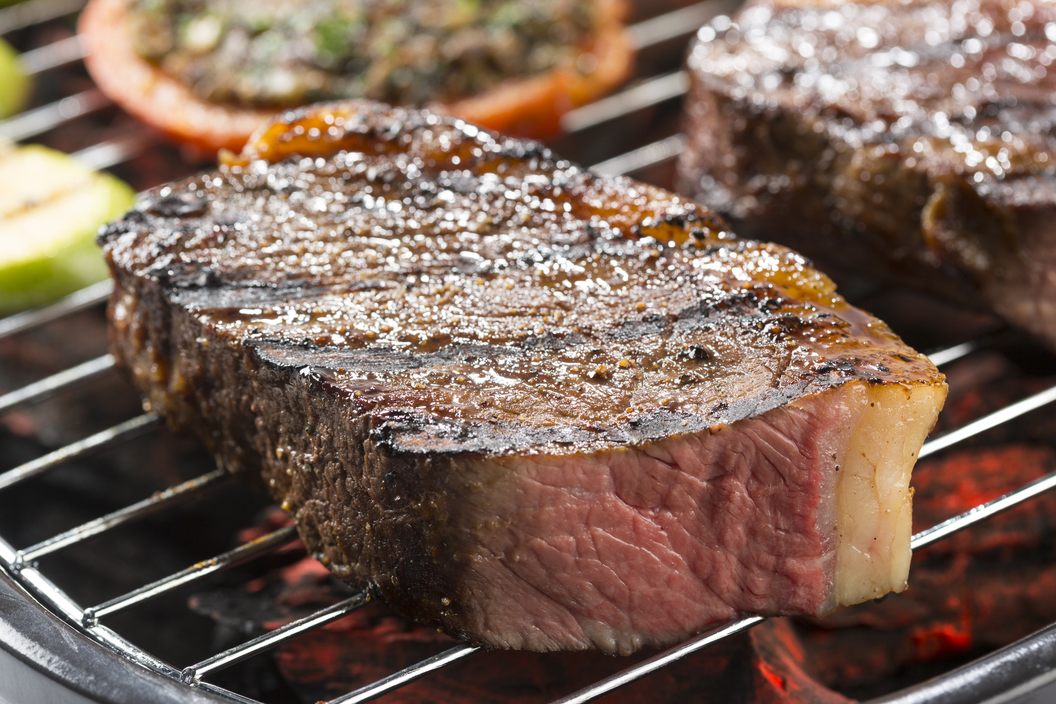 A juicy steak is grilling on an outdoor barbecue, with grill marks visible and a sprinkle of salt on top