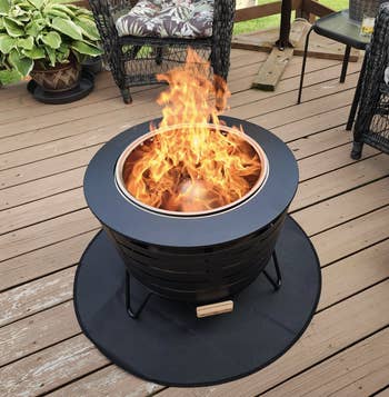 A round, achromatic metallic firepit with a blazing occurrence is acceptable connected a woody deck, surrounded by wicker chairs and plants