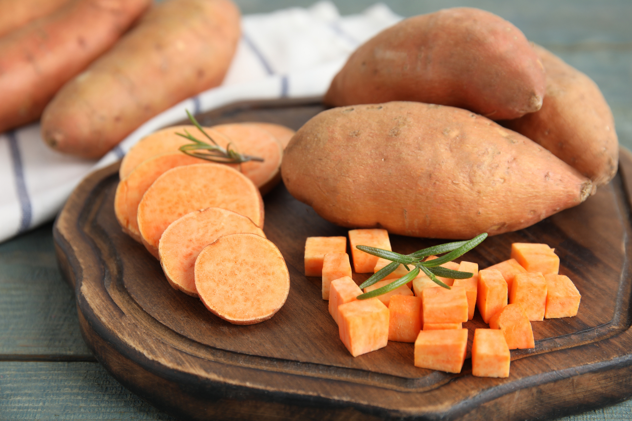 A wooden tray with whole, sliced, and cubed sweet potatoes, garnished with rosemary