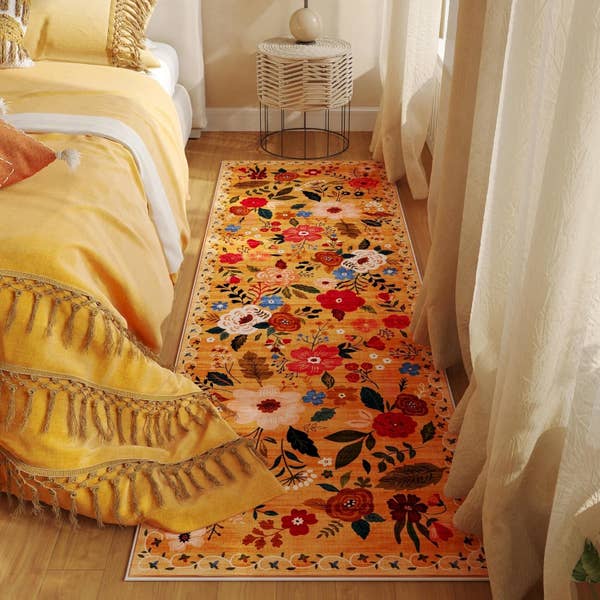Floral-patterned runner rug with red, white, and green accents on a bedroom floor next to a bed with yellow bedding and tassels