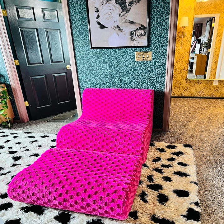 Pink plush lounge chair on a black and white spotted rug in a stylish room with leopard print walls and a black door, along with a black-and-white portrait on the wall