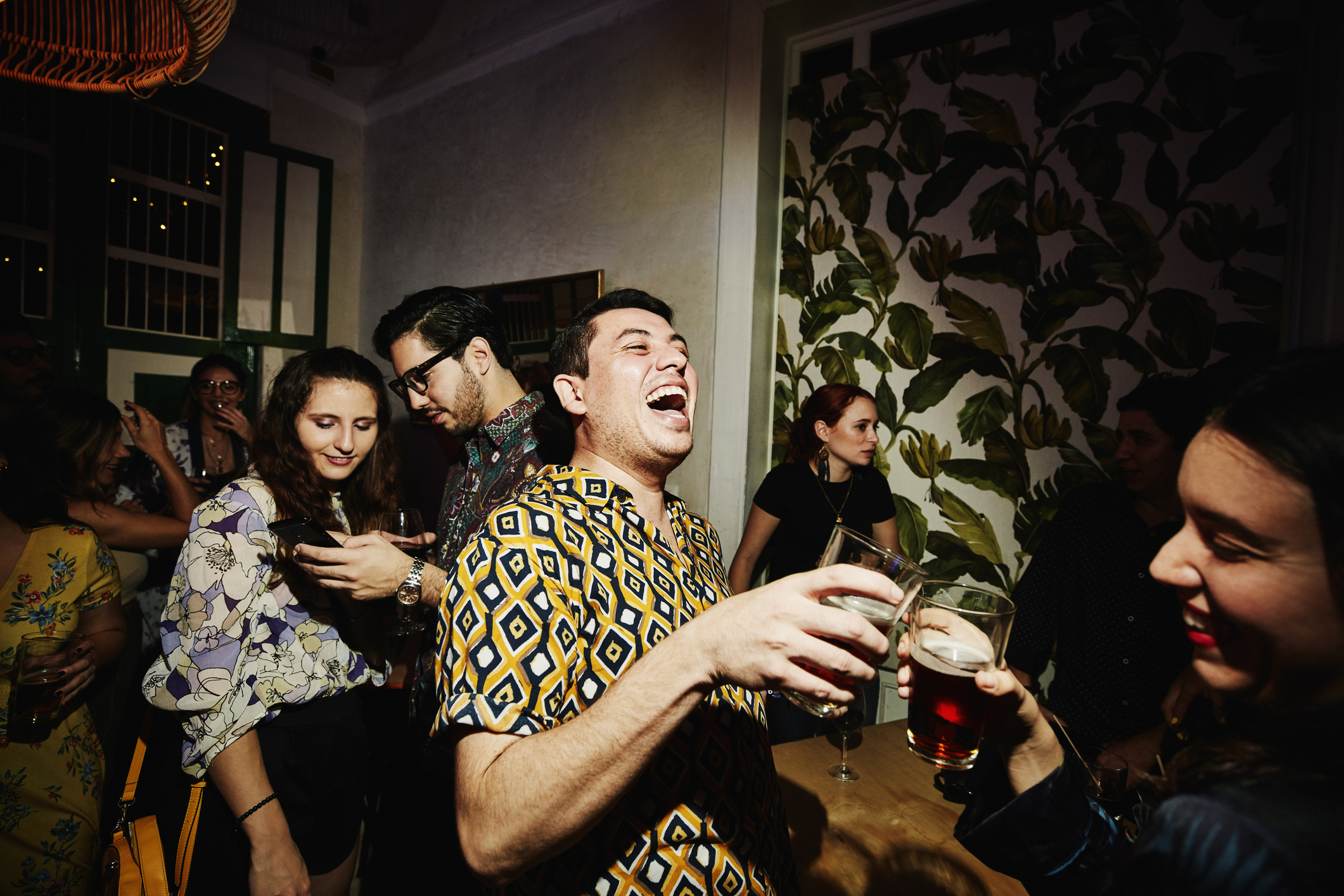 People enjoy a lively party. One man laughs heartily while holding a drink. Others chat and socialize in the background