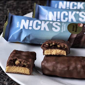 N!CK’S keto snack bars on a white plate, one whole and another cut revealing the filling inside. Packaging is shown in the background
