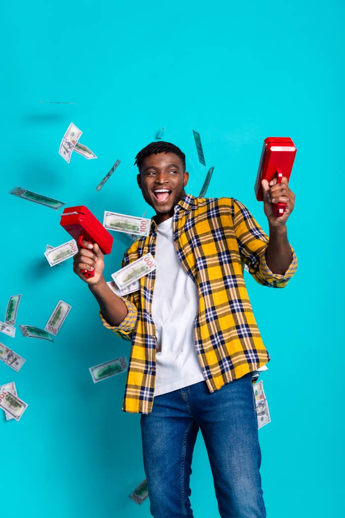 Person in a plaid shirt and jeans joyfully shoots money from red cash guns, with bills floating around them