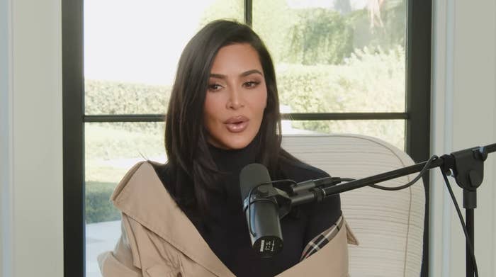 Kim Kardashian speaks into a studio microphone during an interview, wearing a stylish outfit