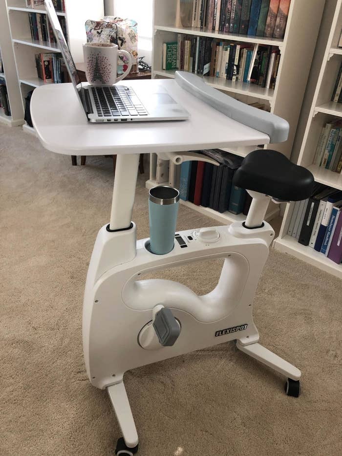 A desk exercise bike with a laptop and coffee cup on the desk surface, positioned in a home library