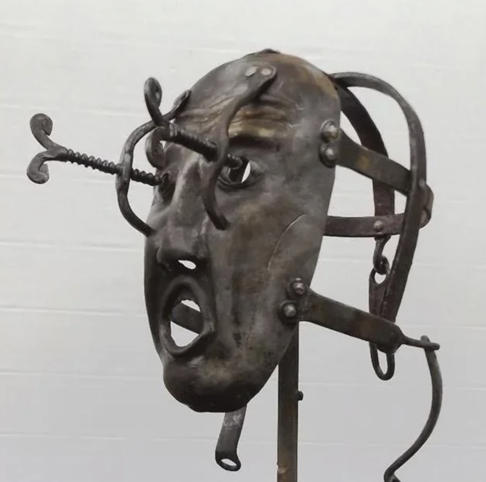A metal mask with a distressed face design, featuring a screw-like element protruding from one eye