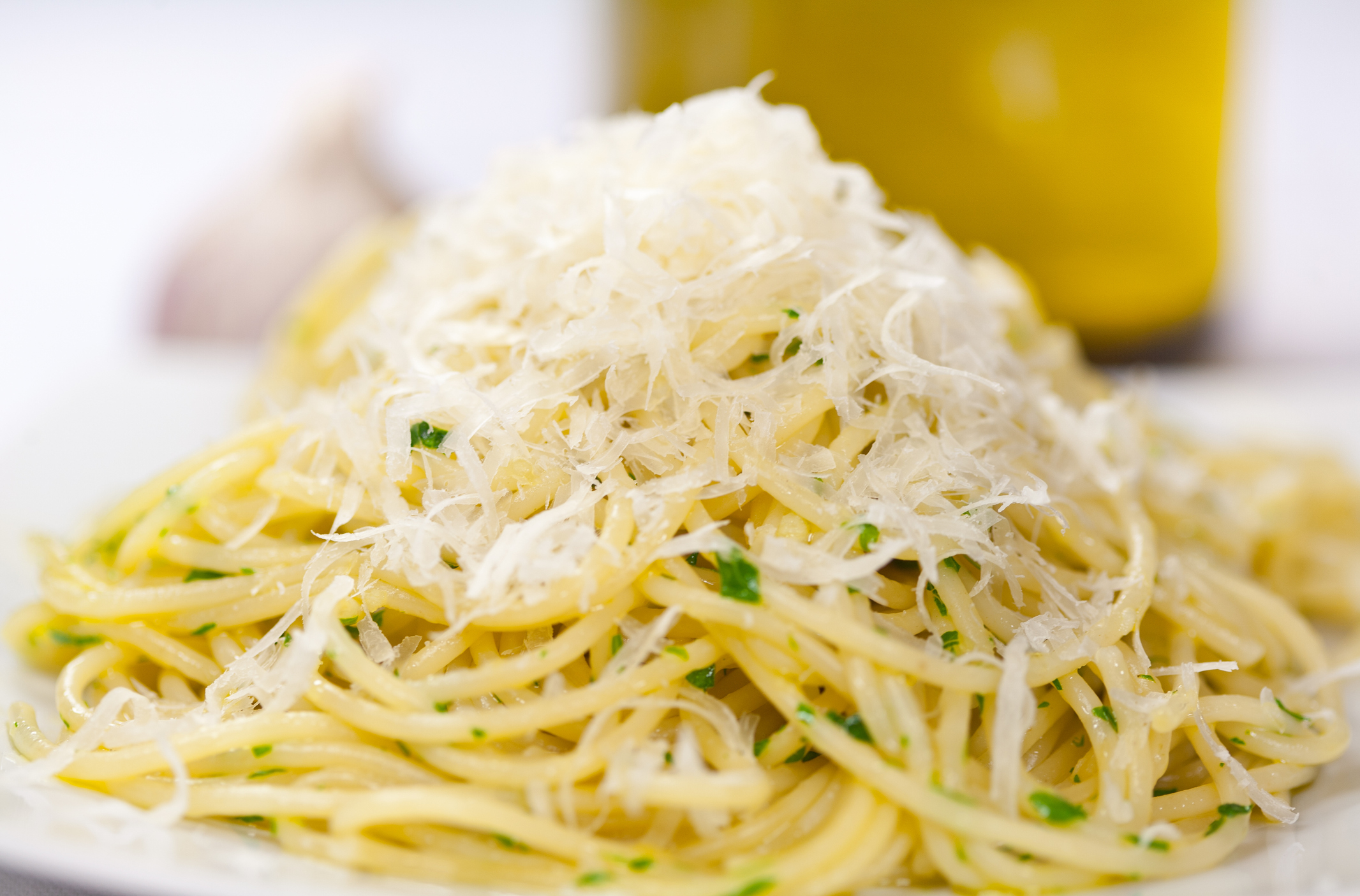 A close-up of a plate of spaghetti aglio e olio with finely grated parmesan cheese on top