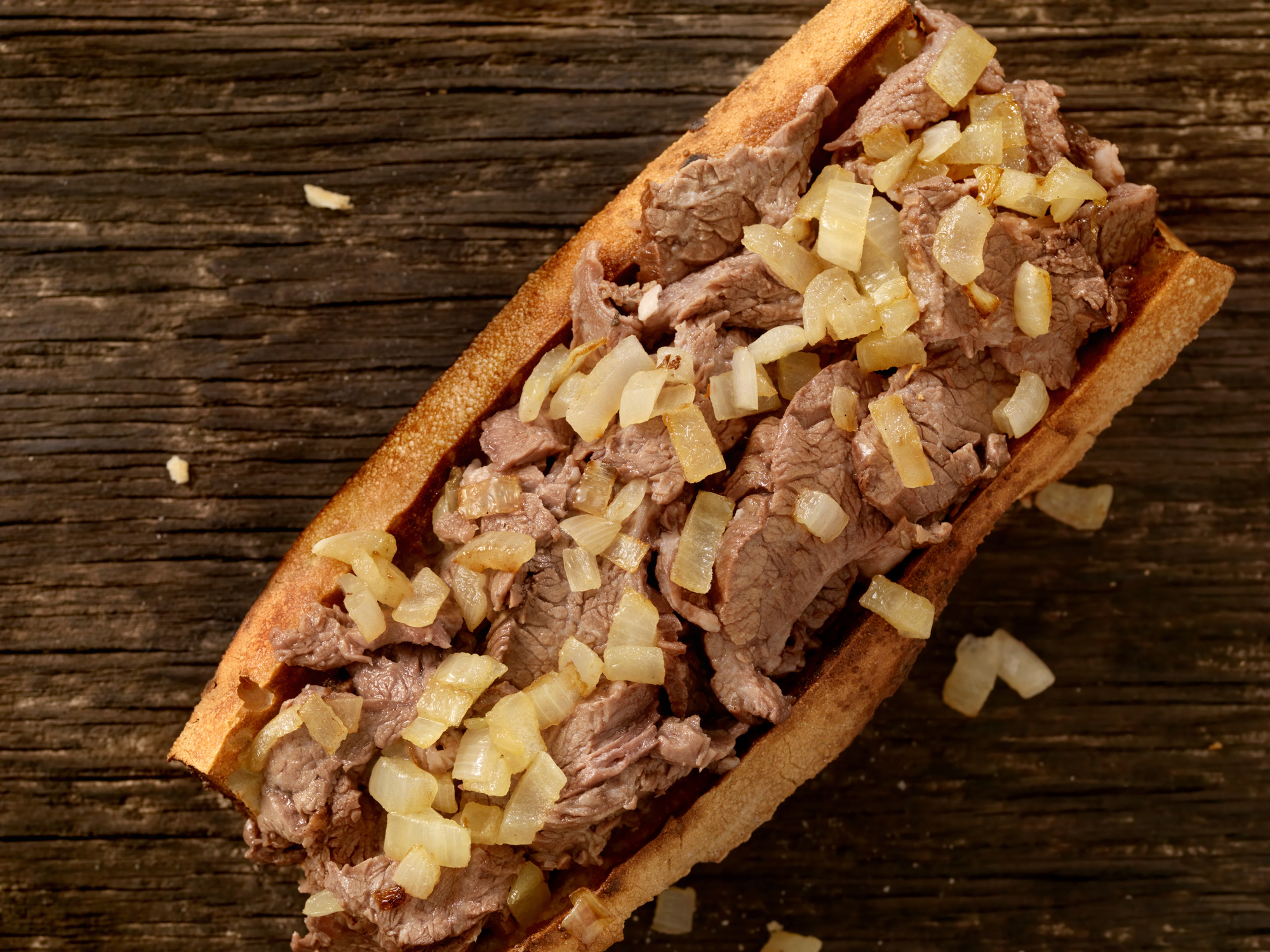 Close-up of a Philly cheesesteak sandwich with sliced beef and sautéed onions on a wooden surface