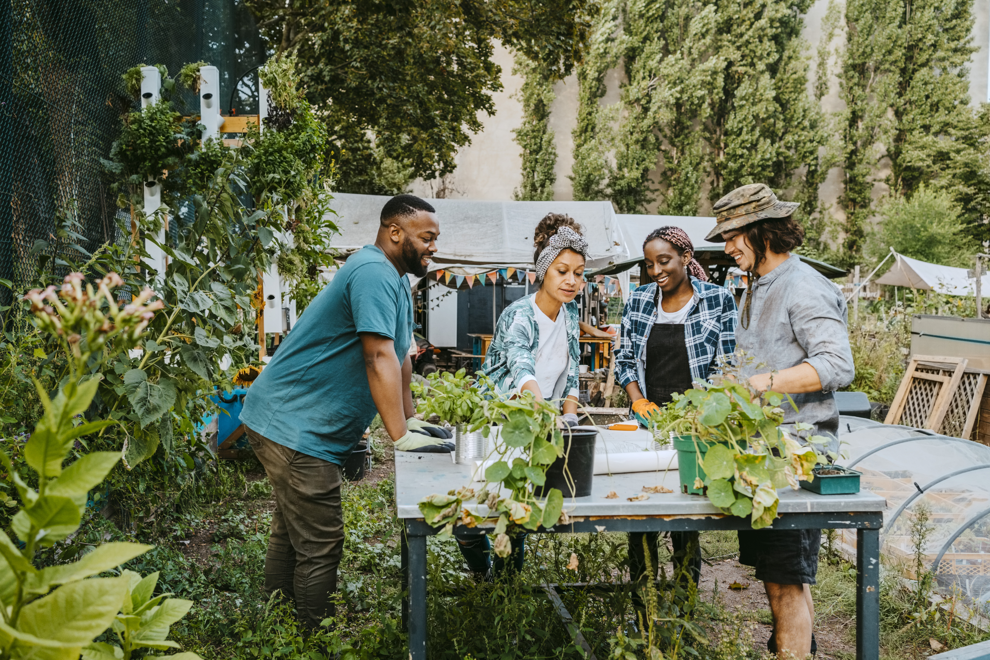 Group of four people gardening together at an outdoor table, surrounded by plants and trees