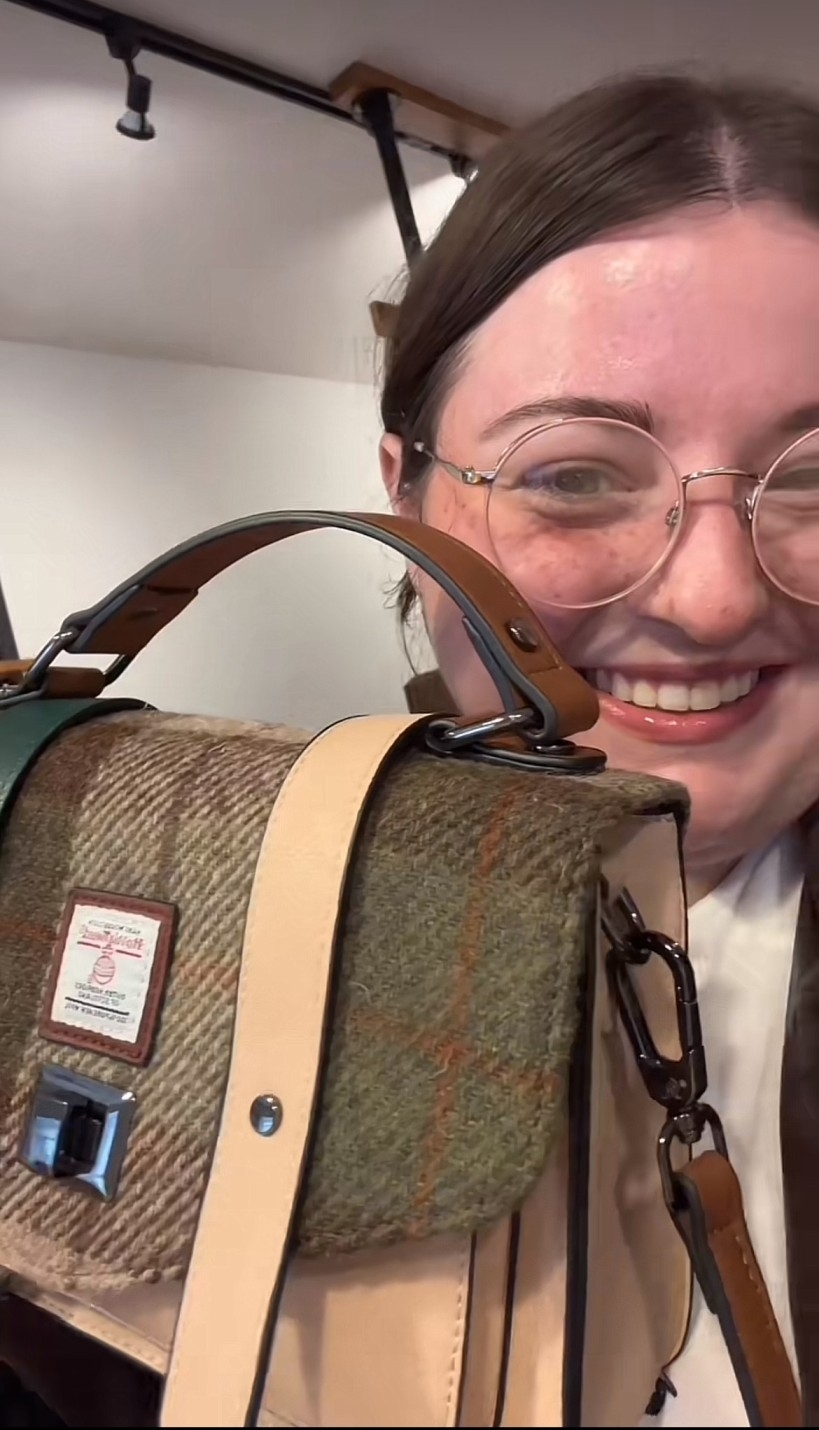 Kristen with glasses and a smile holds a plaid and leather handbag close up for the camera