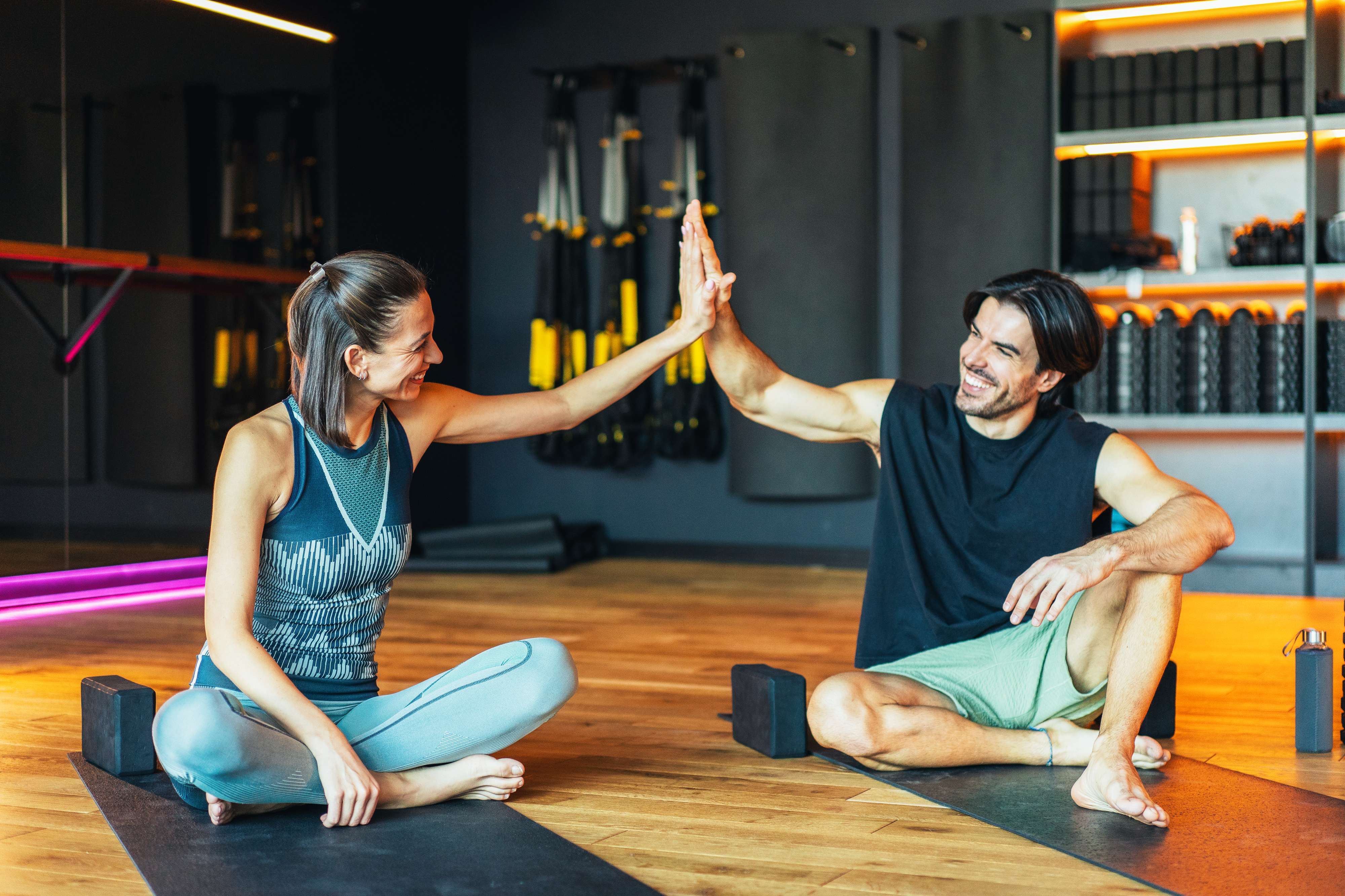 Woman and man sitting on yoga mats in a gym high-fiving each other