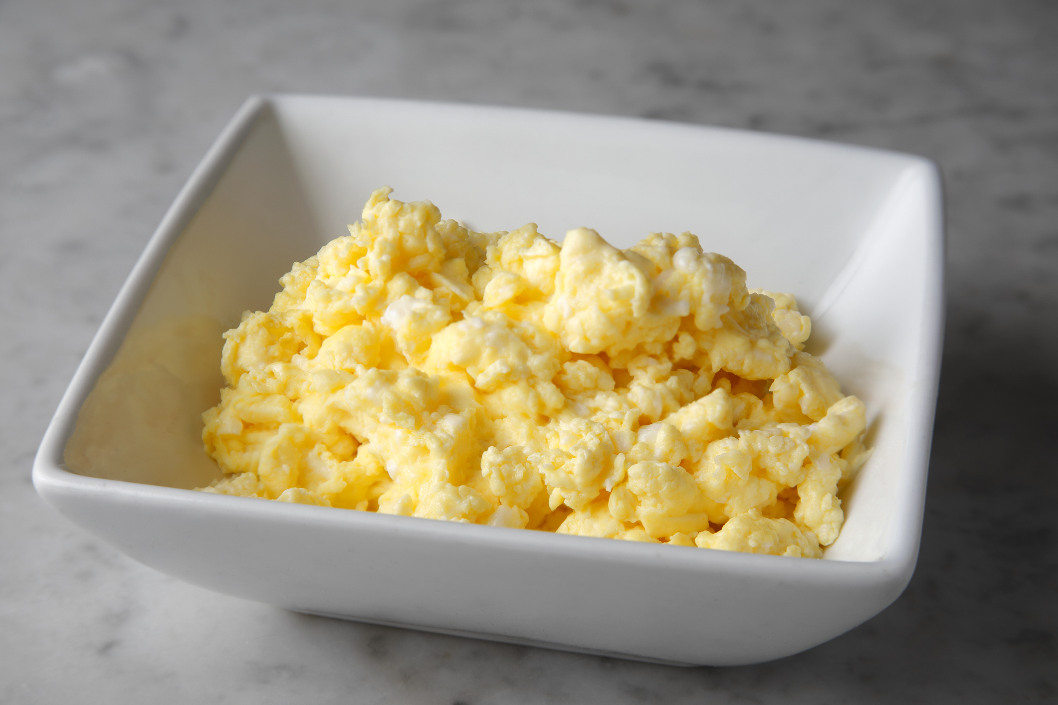 A white bowl filled with scrambled eggs sits on a marble countertop