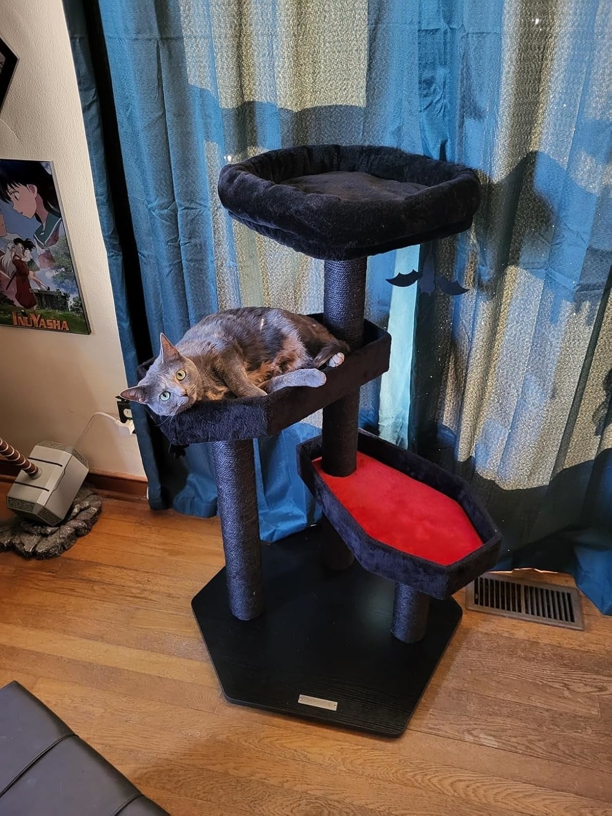 Cat laying on a multi-level cat tree, next to an anime poster, in a room with wooden flooring